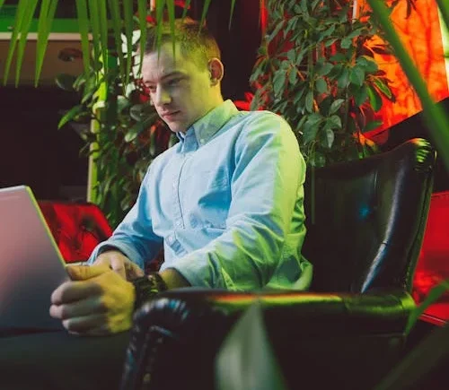 Man in Blue Dress Shirt Sitting on Black Leather Armchair Using Macbook