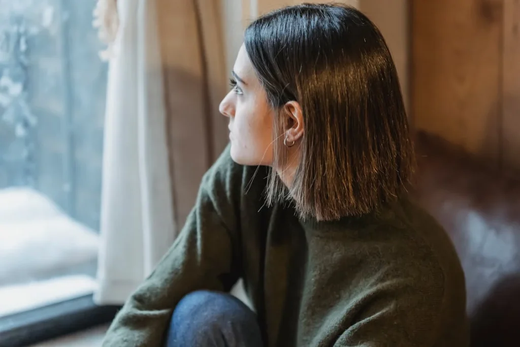 Thoughtful woman sitting on windowsill in solitude